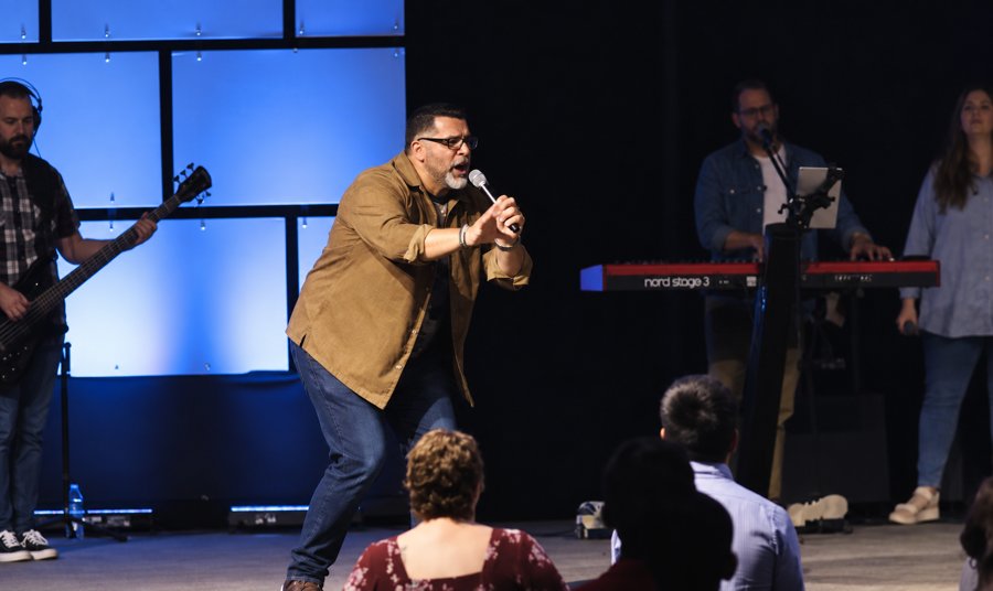 Manny Rivera preaching on stage with worship team